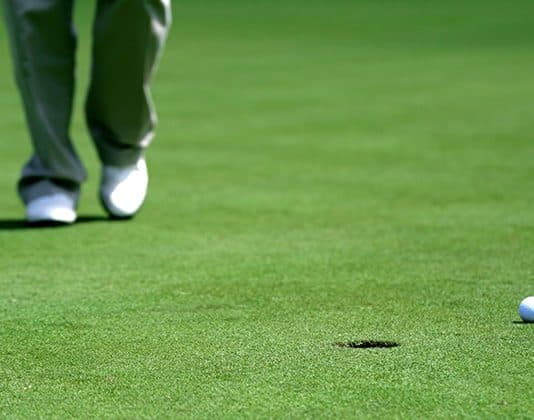 A golfer with a club approaching a putt